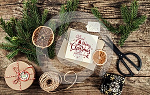 Merry Christmas card with fir branches, gifts on wooden background with scissors and skein of jute. Xmas and Happy New Year theme,