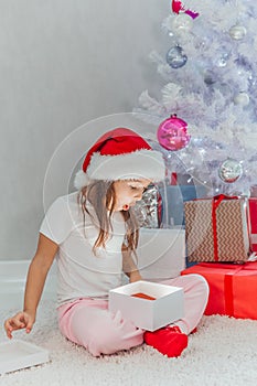 Merry Christmas celebration. Cheerful beautiful little girl sitting near the Christmas tree holding a gift box