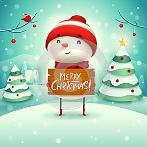 Merry Christmas! Cheerful snowman holds wooden board sign in Christmas snow scene winter landscape.