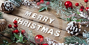 Merry Christmas composition. Fir branches with cones, berries and snow decorations on old dark wooden background with letters text