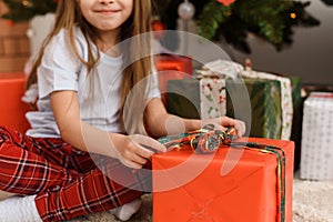 Merry Christmas. Cute little girl opens a present near the Christmas tree. The girl enjoys the gift.