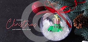Merry christmas on dark background with transparent christmas ball with a toy car gift on the roof in the snow
