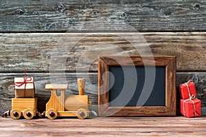 Merry Christmas decorations, empty chalkboard with toy wooden train and christmas gifts on a timber background