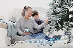 Merry christmas family at home, smiling brother and sister decorate the tree hang blue balls and snowflake decoration sitting on