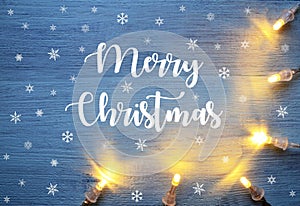 Merry Christmas festive background with garland lights on a blue wooden board.Winter holidays greeting card.