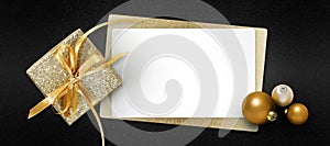 Merry christmas gift card with golden box with ribbon bow, white ticket and silver balls isolated on black glitter background, top