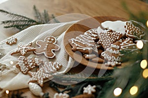 Merry Christmas! Gingerbread cookies with icing in plate on wooden rustic table with fir branches, festive decorations and