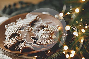 Merry Christmas! Gingerbread cookies with icing in plate on wooden rustic table with fir branches, festive decorations and