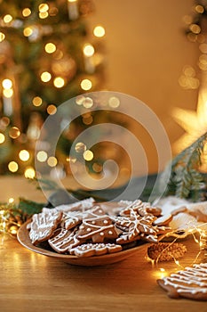 Merry Christmas! Gingerbread cookies with icing in plate on wooden table with fir branches and festive decorations against