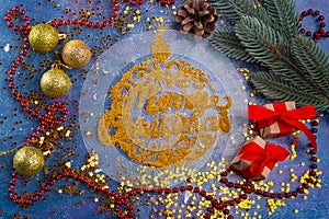 Merry Christmas golden words written by glowing glitter in shape of decoration ball. Top view on red beads, golden balls, small