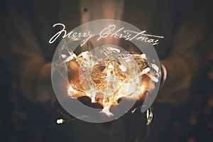 Merry christmas greeting card - led lights garland glowing in woman hands