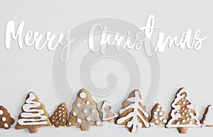 Merry Christmas Greeting card. Merry Christmas text handwritten on christmas trees gingerbread cookies on white wooden background