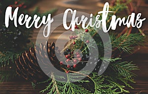 Merry Christmas Greeting card. Merry Christmas text handwritten on modern rustic christmas wreath on wooden table with red berries