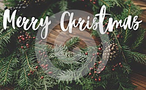 Merry Christmas Greeting card. Merry Christmas text handwritten on rustic christmas wreath on wooden table. Happy holidays,