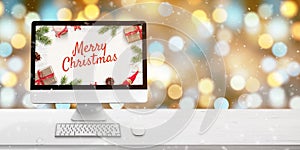 Merry Christmas greeting on computer display on white wooden desk. Bokeh and Christmas lights in background