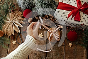 Merry Christmas! Hands tying ribbon on christmas oatmeal cookies on background of stylish festive decorations on rustic wooden