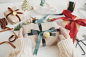 Merry Christmas! Hands wrapping stylish christmas gift. Person preparing  christmas present with green ribbon and ornaments