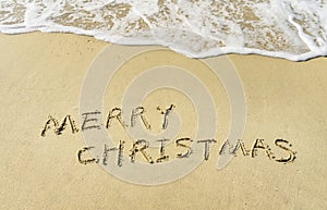 Merry Christmas handwritten in sand on beach