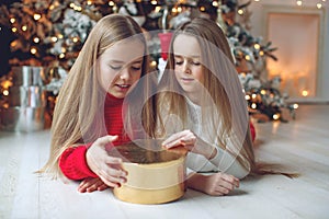 Merry Christmas and Happy Holidays. Cheerful cute kid girls opening gifts. Children near the tree in the morning.