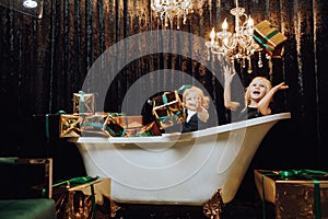 Merry Christmas and Happy Holidays! Cheerful girl and boy in a bath with Christmas gifts in gold wrappers.