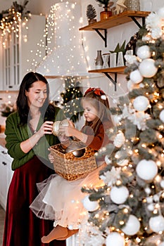 Merry Christmas and Happy Holidays. Cheerful mom and her cute daughter decorating and having fun near Christmas tree