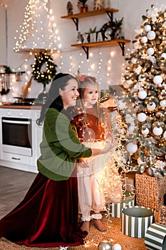 Merry Christmas and Happy Holidays. Cheerful mom and her cute daughter decorating and having fun near Christmas tree