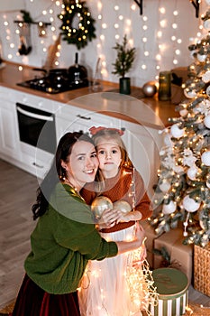 Merry Christmas and Happy Holidays. Cheerful mom and her cute daughter decorating and having fun near Christmas tree