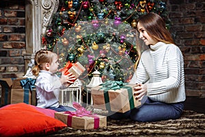 Merry Christmas and Happy Holidays! Cheerful mom and her cute daughter exchanging gifts. Parent and little child having fun near C