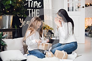 Merry Christmas and Happy Holidays. Cheerful mom and her cute daughter girl opening a Christmas present. Parent and
