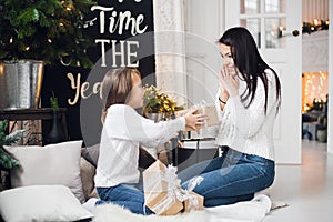 Merry Christmas and Happy Holidays. Cheerful mom and her cute daughter girl opening a Christmas present. Parent and