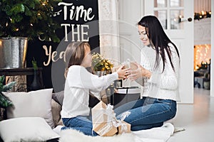 Merry Christmas and Happy Holidays. Cheerful mom and her cute daughter girl opening a Christmas present. Parent and