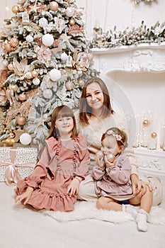Merry Christmas and Happy Holidays. Cheerful mom and her cute daughters girls hugging and smiling on sofa. Parent and