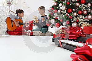 Merry christmas and happy holidays, children play guitar and tambourine near the christmas tree with wrapped gift packages and