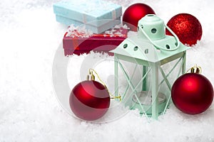 Merry Christmas and Happy Holidays concept with red baubles, gift boxes and a green lantern on snow with copy space