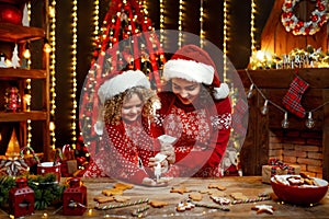 Merry Christmas and Happy Holidays. Cheerful cute curly little girl and her older sister in santas hats cooking