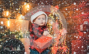 Merry Christmas and happy holidays. Funny baby is opening a Christmas gift in his hands on the Christmas background