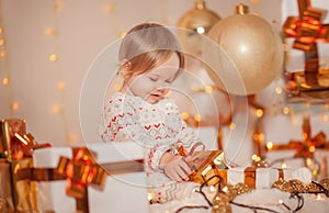 Merry Christmas and Happy Holidays! Little cute kid girl sitting in decorated room holding present box with surprise and smiling.