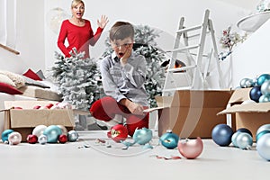 Merry Christmas and Happy Holidays! Mom and son decorate the Christmas tree indoors. accidentally the child breaks the balls,