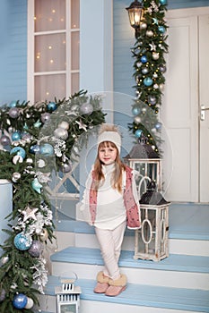 Merry Christmas, happy holidays! New Year 2020. little girl stands on porch of house decorated for Christmas. child decorates terr