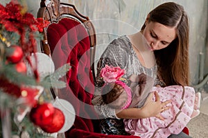 Merry Christmas and Happy Holidays Pretty young mom reading a book to her cute daughter near Christmas tree indoors