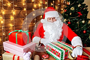 Merry Christmas and Happy Holidays. Santa Clause is preparing gifts for children for Xmas at desk at home.