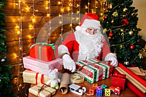 Merry Christmas and Happy Holidays. Santa Clause is preparing gifts for children for Xmas at desk at home.