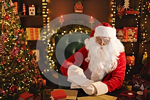 Santa Clause is prepares gifts for children for Xmas at his desk while reading wish lists