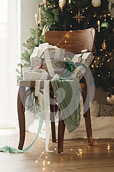 Merry Christmas and Happy Holidays! Stylish wrapped christmas gifts with ribbon on wooden old chair on background of decorated