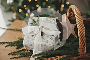 Merry Christmas and Happy holidays! Stylish wrapped christmas gift, rustic basket with fir branches and modern decorations against