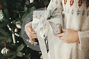 Merry Christmas and happy holidays! Woman holding stylish christmas gift with ribbon and fir branch close up on background of