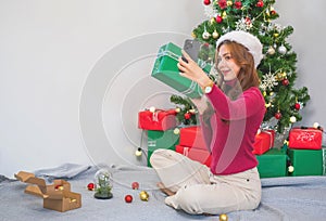 Merry Christmas and Happy Holidays! Young woman with a beautiful face in a red shirt shows joy with gift boxes in a house with a
