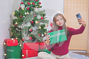 Merry Christmas and Happy Holidays! Young woman with a beautiful face in a red shirt shows joy with gift boxes in a house with a