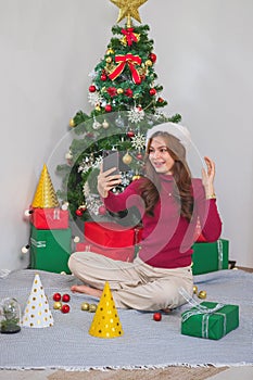 Merry Christmas and Happy Holidays! Young woman with a beautiful face in a red shirt shows joy with gift boxes in a house with a