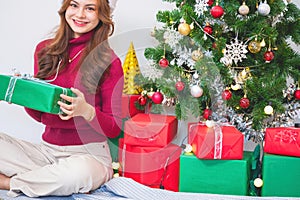 Merry Christmas and Happy Holidays! Young woman with a beautiful face in a red shirt shows joy with gift boxes in a house with a